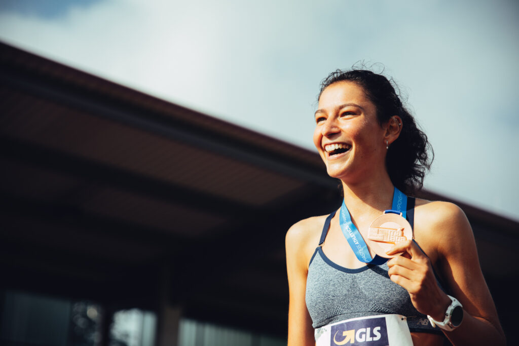 Sportlerin hält stolz lächelnd eine Medaille hoch